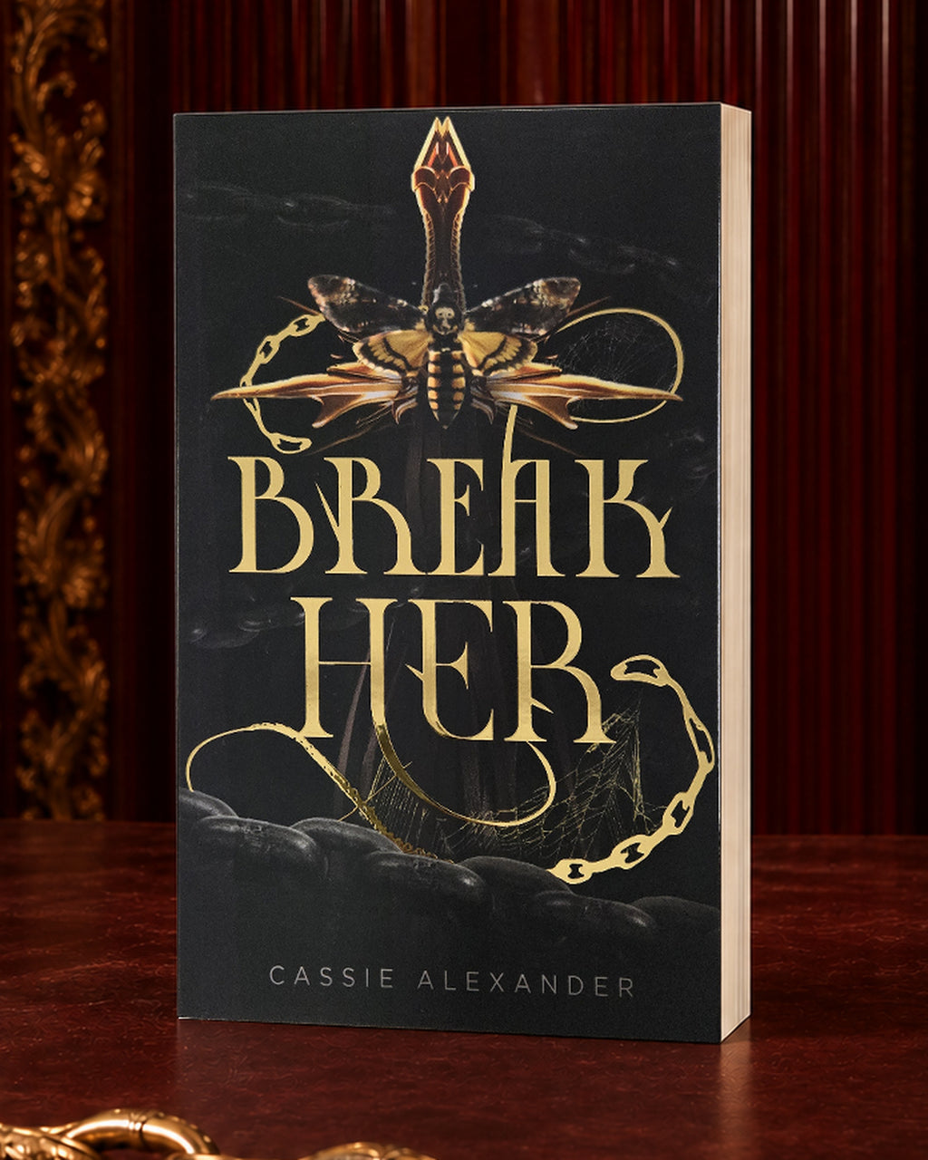 Break Her black-and-gold foil paperback in an oxblood editorial setting