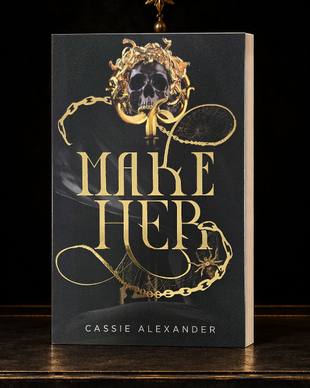 Make Her black-and-gold foil paperback in a dark gilded vault